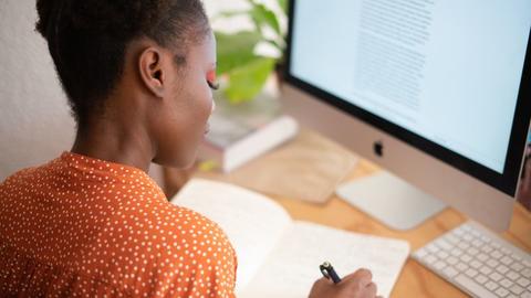 Women writing in planner with computer screen in background